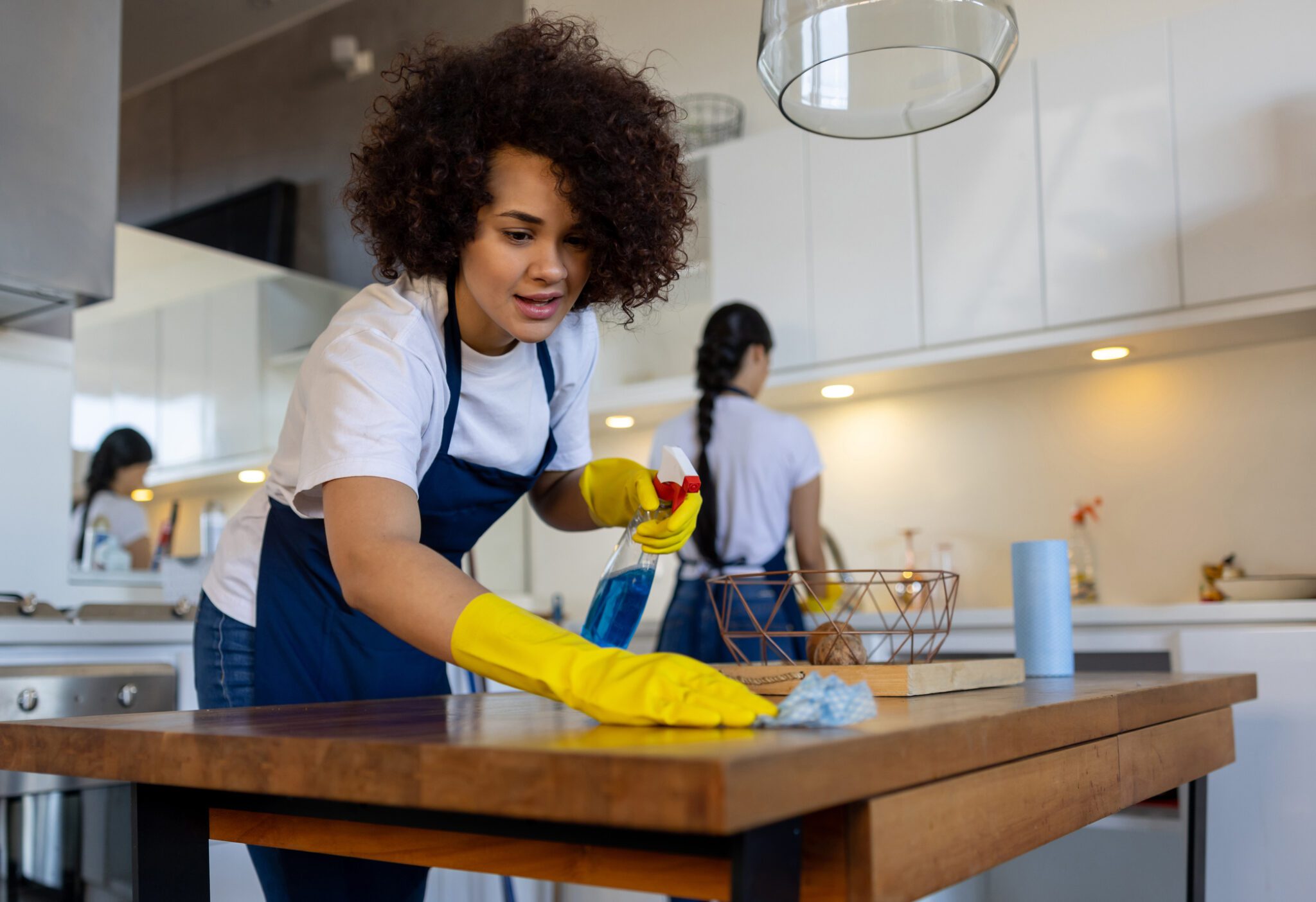 Woman cleaning kitchen table with spray bottle.