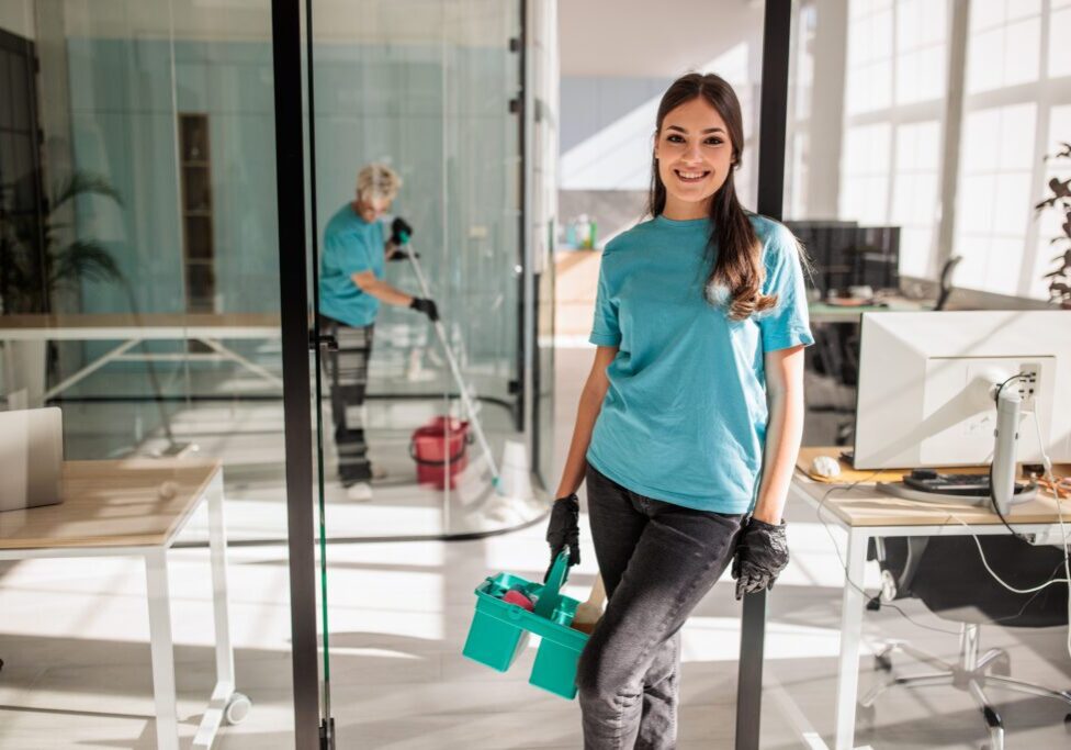 Young woman from a professional cleaning team standing proudly in a sleek, contemporary office space